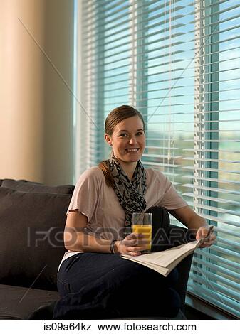 Stock Photo - Woman reading newspaper on sofa. Fotosearch