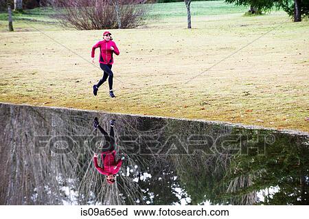 Stock Image - Woman running by still rural lake. Fotosearch