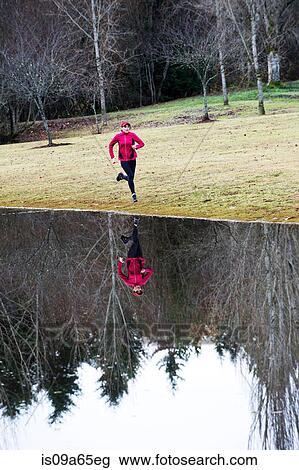 Stock Image - Woman running by still rural lake. Fotosearch