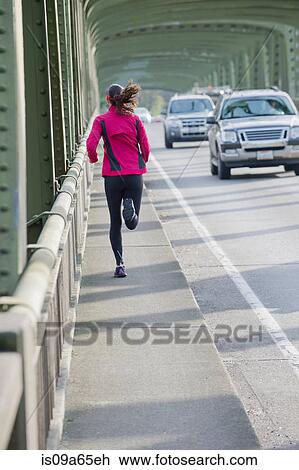 Stock Image - Woman running on urban bridge. Fotosearch