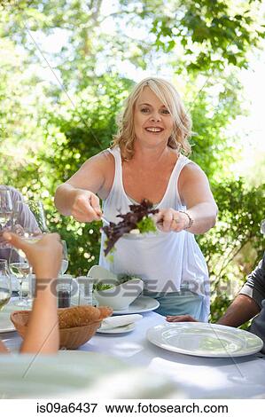 Stock Photo - Woman serving salad at table outdoors. Fotosearch