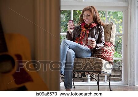 Stock Image - Woman using cell phone in armchair. Fotosearch