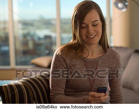 Picture - Woman using cell phone on sofa. Fotosearch