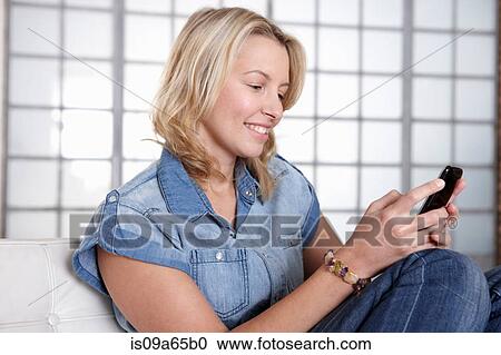 Stock Image - Woman using cell phone on sofa. Fotosearch