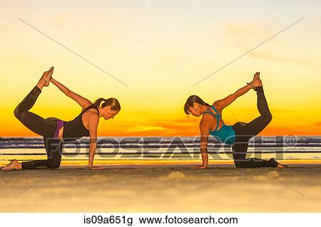 Stock Image - Women practicing yoga on beach. Fotosearch