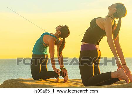 Stock Image - Women practicing yoga on rock formation. Fotosearch