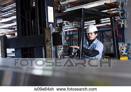 Stock Image - Worker driving forklift in metal plant. Fotosearch