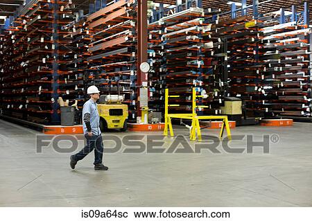 Stock Image - Worker walking in metal plant. Fotosearch