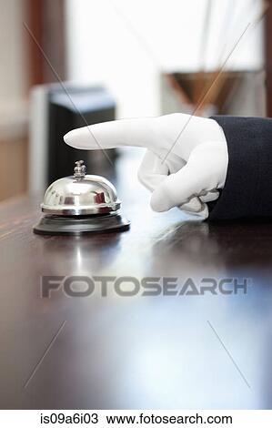 Stock Image - Bellhop ringing bell in hotel lobby. Fotosearch