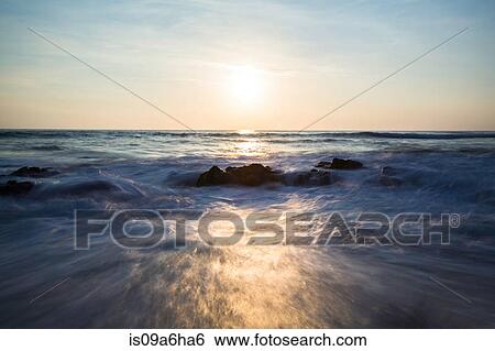 Stock Photograph - Blurred view of waves on rocky beach. Fotosearch