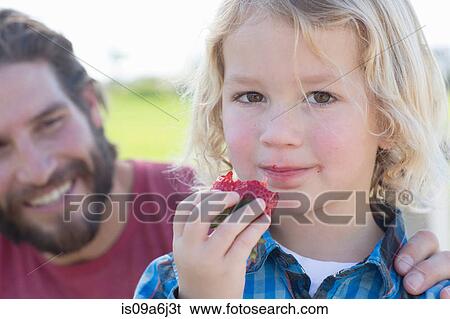Stock Photograph - Boy eating strawberry outdoors. Fotosearch