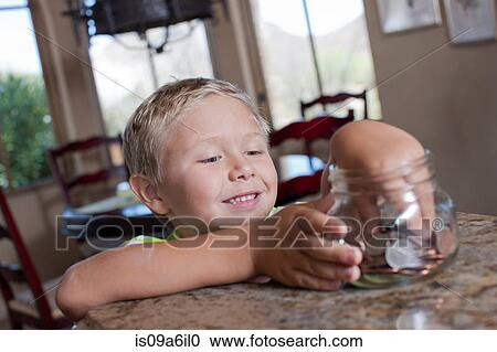Stock Image - Boy putting savings in glass jar. Fotosearch