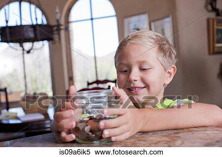 Stock Photography - Boy putting savings in glass jar. Fotosearch