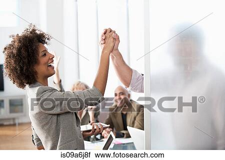 Stock Image - Business people shaking hands in office. Fotosearch