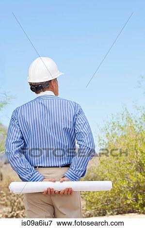 Stock Photo - Businessman in hard hat with blueprints. Fotosearch