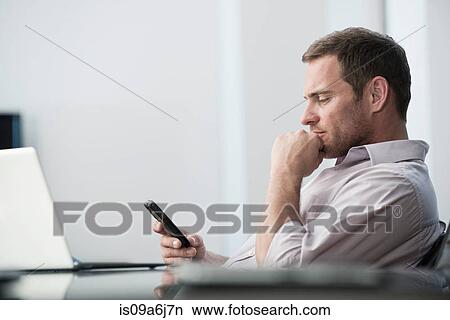 Picture - Businessman using cell phone at desk. Fotosearch