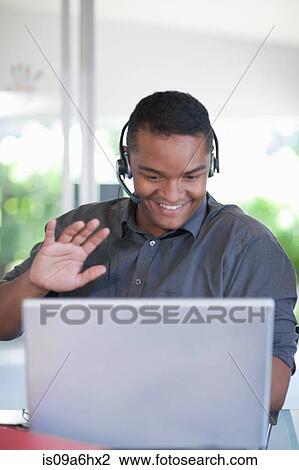 Stock Image - Businessman wearing headset at desk. Fotosearch