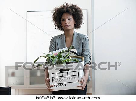 Stock Image - Businesswoman packing up box in office. Fotosearch