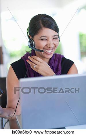Stock Image - Businesswoman wearing headset at desk. Fotosearch