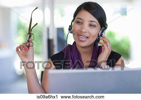 Stock Image - Businesswoman wearing headset at desk. Fotosearch