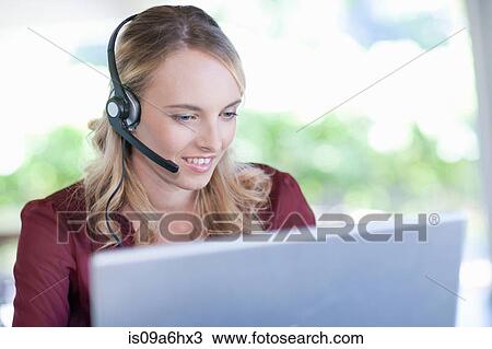 Stock Image - Businesswoman wearing headset at desk. Fotosearch