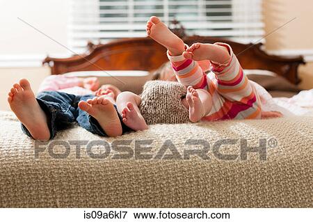 Stock Photo - Children laying with infant on bed. Fotosearch