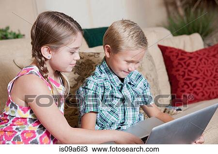 Stock Image - Children using laptop together on sofa. Fotosearch