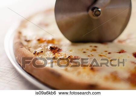 Stock Photograph - Close up of cutter slicing pizza. Fotosearch