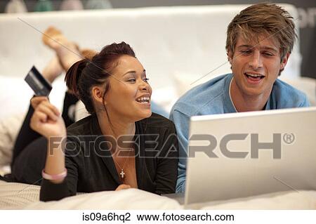 Stock Image - Couple shopping online in bed. Fotosearch