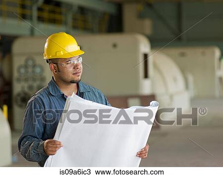Stock Image - Engineer reading blueprints on site. Fotosearch