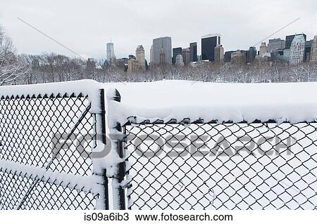 Stock Image - Fence, snowy urban park and skyline. Fotosearch