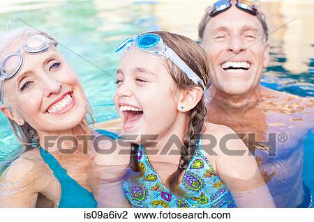 Stock Image - Girl and grandparents swimming in pool. Fotosearch