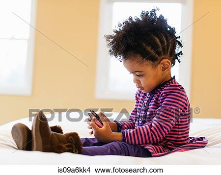 Girl playing with cell phone on bed View Large Photo Image Picture - Girl playing with cell phone on bed. Fotosearch
