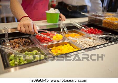 Stock Image - Girl putting toppings on frozen yogurt. Fotosearch