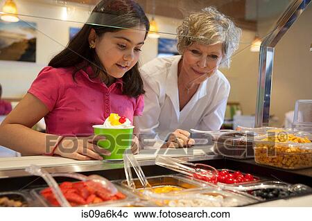 Stock Image - Girl putting toppings on frozen yogurt. Fotosearch