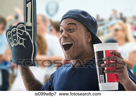 Man at sports game with foam hand and soft drink cup View Large Photo Image Stock Photo - Man at sports game with foam hand and soft drink cup. Fotosearch