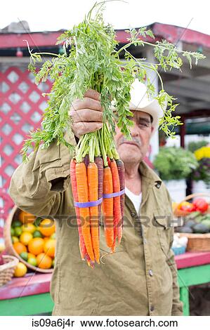 Stock Photography - Man holding carrots at farmer's market. Fotosearch