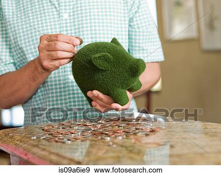 Stock Photo - Man putting coins in green piggy bank. Fotosearch