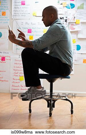 Man sitting on stool with digital tablet View Large Photo Image Stock Image - Man sitting on stool with digital tablet. Fotosearch