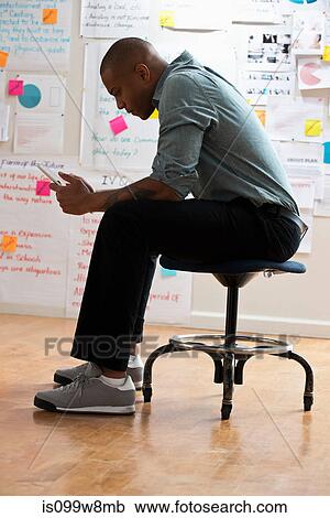 Man sitting on stool with digital tablet View Large Photo Image Stock Image - Man sitting on stool with digital tablet. Fotosearch