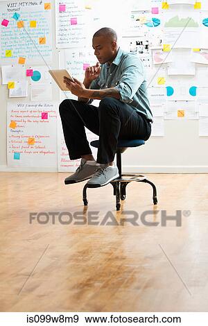 Man sitting on stool with digital tablet View Large Photo Image Stock Photo - Man sitting on stool with digital tablet. Fotosearch