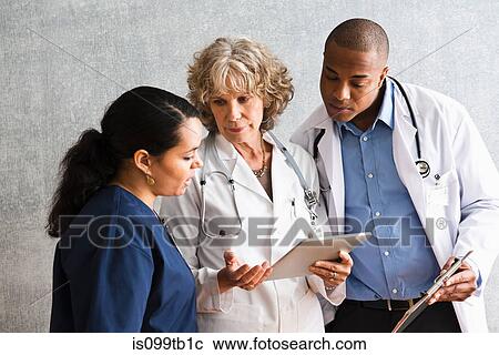 Stock Image - Nurse and doctors talking with digital tablet. Fotosearch