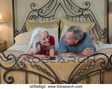 Stock Image - Older couple reading on bed. Fotosearch