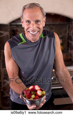 Stock Image - Older man having fruit in kitchen. Fotosearch