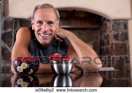 Stock Image - Older man having fruit in kitchen. Fotosearch