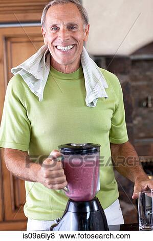 Stock Photo - Older man making smoothie in kitchen. Fotosearch
