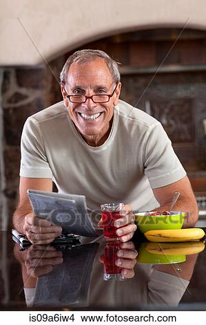 Picture - Older man reading newspaper at breakfast. Fotosearch