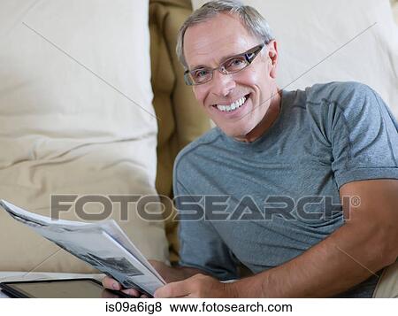 Stock Photo - Older man reading newspaper on bed. Fotosearch