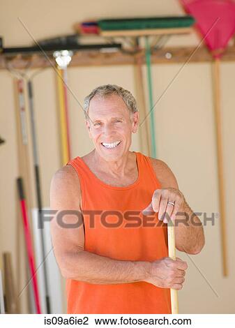 Stock Image - Older man sweeping garage. Fotosearch