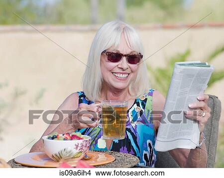 Picture - Older woman having breakfast outdoors. Fotosearch